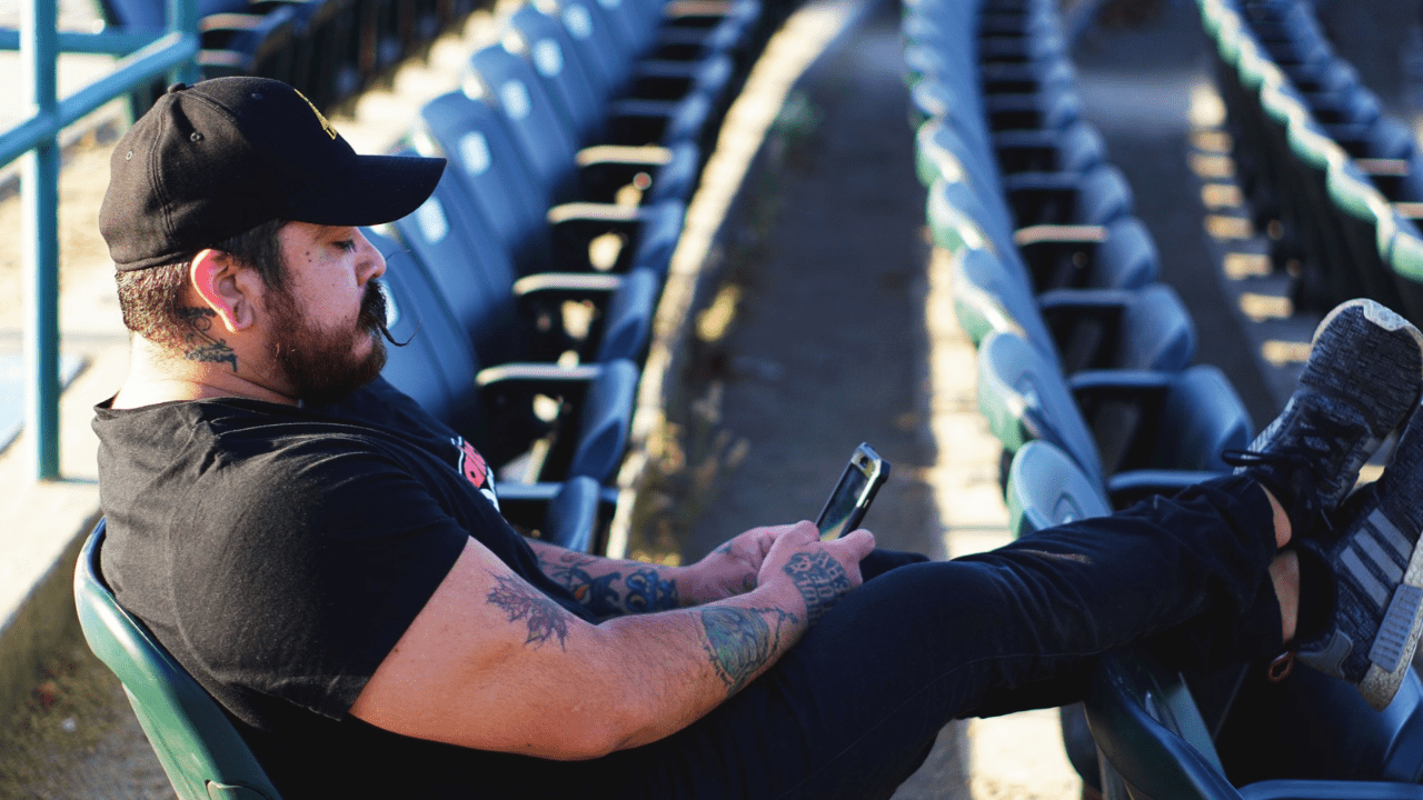 Man sitting on stadium bleachers while looking at his smartphone