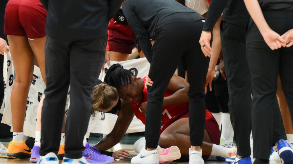Aliyah Boston injury image showing Boston on the floor surrounded by trainers and teammates after hurting her apparent leg during the Fever–Storm game.