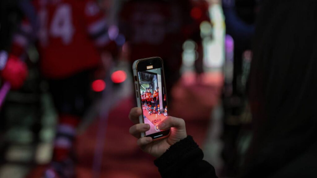 Fan records a sports event on a smartphone, illustrating the online persona element of the Daejon Love scam allegations