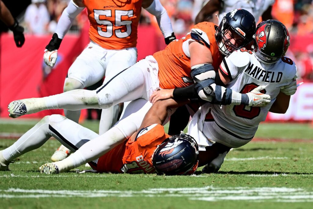 Buccaneers Quarterback Baker Mayfield being sacked by numerous Denver Broncos defenders.